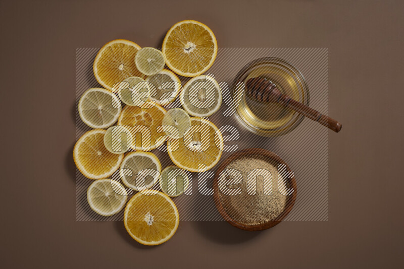 Two bowls full of honey and ground ginger with some of citrus fruits such as lemon and orange on a beige background