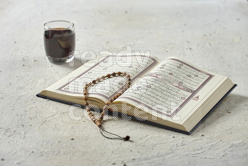 Quran with dates, prayer beads and different drinks all placed on textured white background