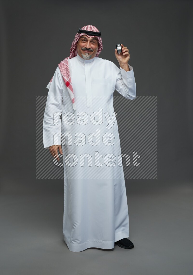 Saudi man with shomag Standing holding car key on gray background