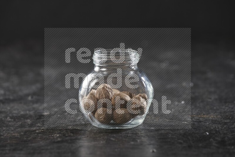 A glass spice jar full of whole nutmeg seeds on a textured black flooring