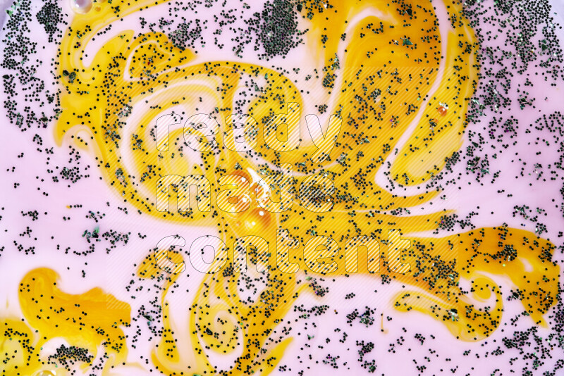 A close-up of sparkling green glitter scattered on swirling yellow and pink background