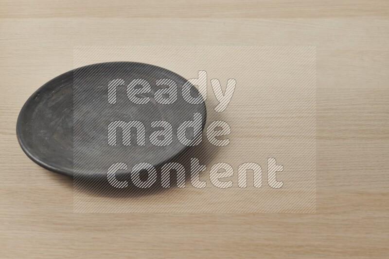 A circular black pottery plate on light wooden background