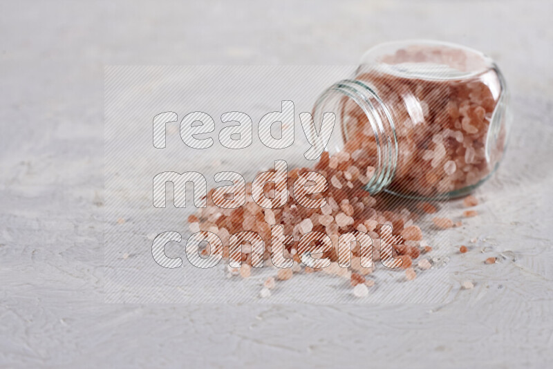 A glass jar full of coarse himalayan salt crystals on white background