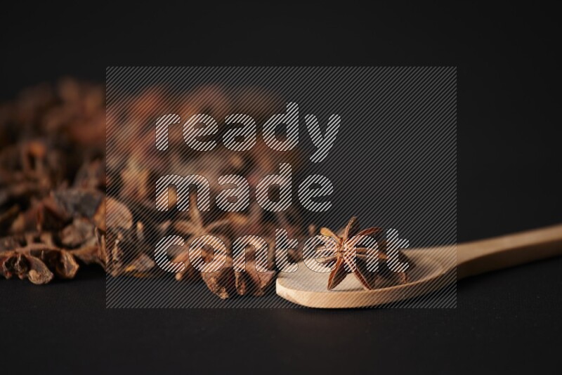 اليانسون النجمي في ملعقة خشبية ومتناثر على أرضية سوداء