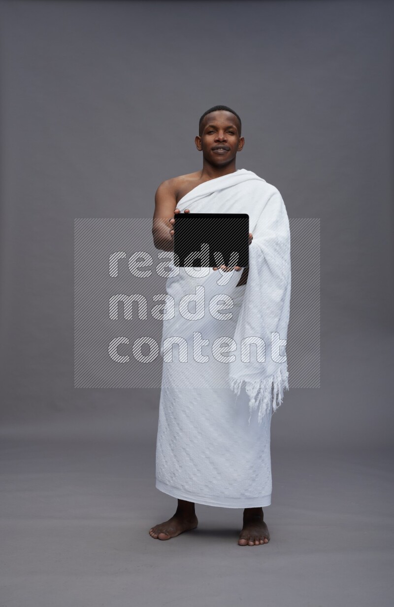 A man wearing Ehram Standing showing tablet to camera on gray background