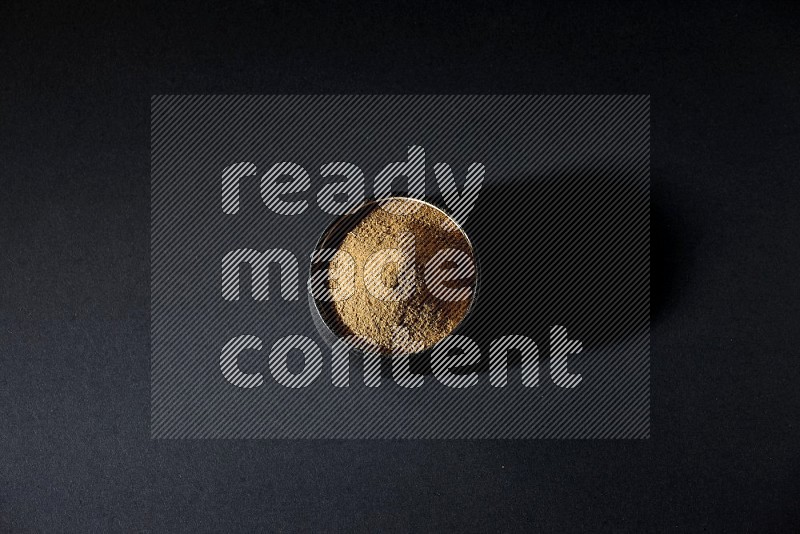 A black pottery bowl full of cumin powder on a black flooring