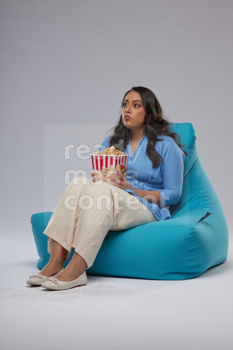 A woman sitting on a blue beanbag and eating popcorn