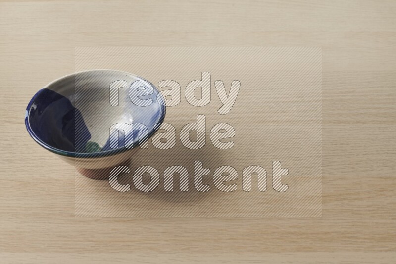 A multicolored pottery bowl on light wooden background