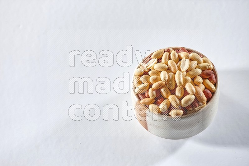 A beige ceramic bowl full of peeled peanuts on a white background in different angles