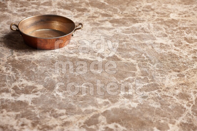 A small copper pan on beige marble background