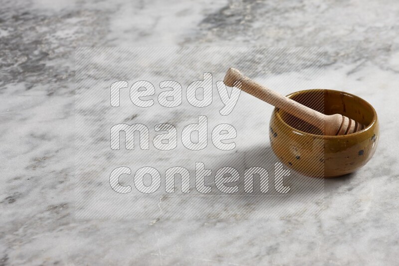 Multicolored pottery bowl with wooden honey dipper in it on grey marble background