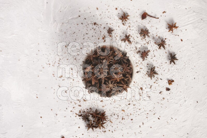 اليانسون النجمي في وعاء أبيض والمزيد من اليانسون متناثر على خلفية بيضاء