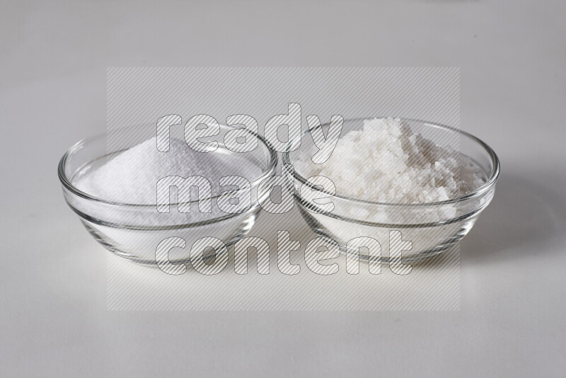 2 glass bowls one is filled with table salt and the other with coarse sea salt on white background