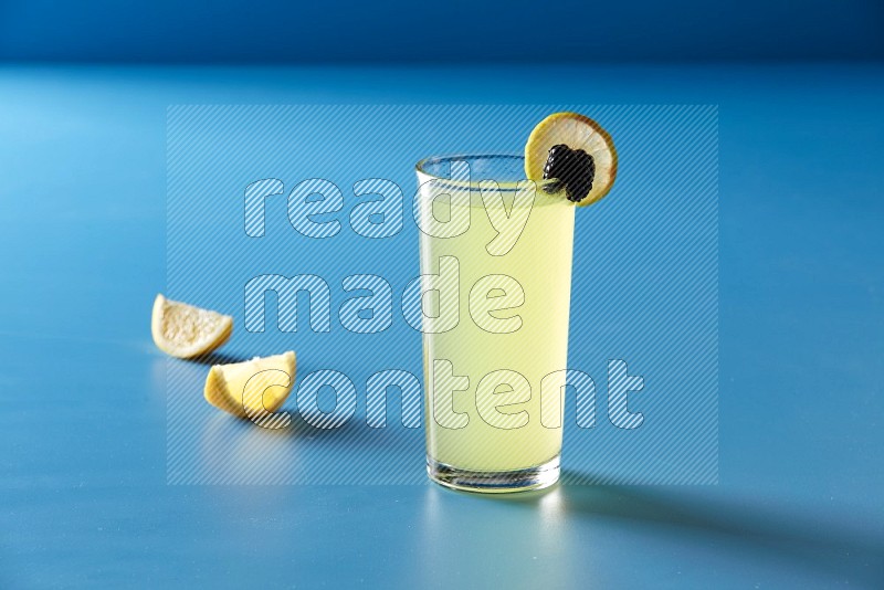 glass of lemon juice with lemon slice and berry on blue background