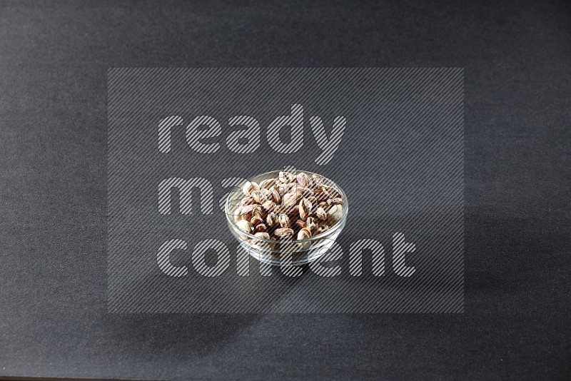 A glass bowl full of peeled pistachios on a black background in different angles