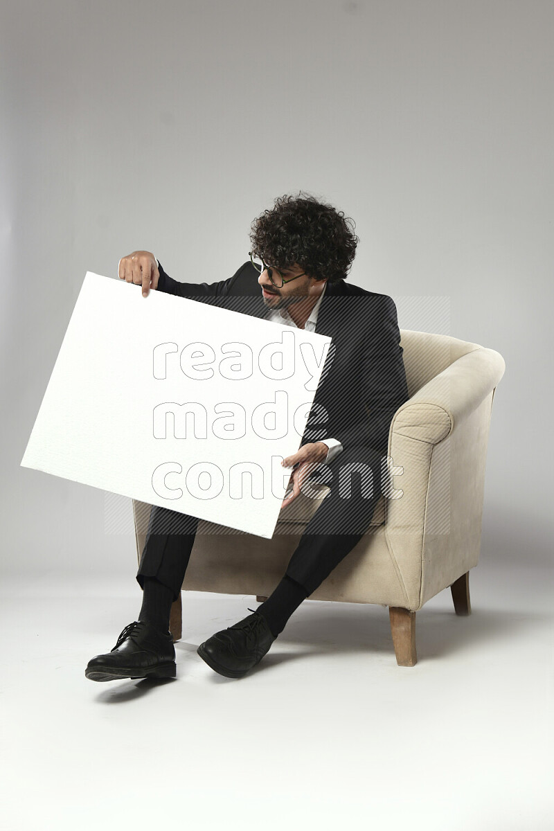 A man wearing formal sitting on a chair holding a white board on white background