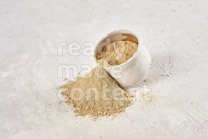 A beige pottery bowl full of ground ginger powder with fallen powder from it on white background