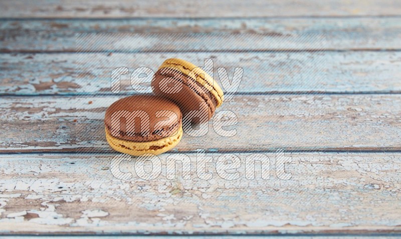 45º Shot of two Yellow and Brown Chai Latte macarons on light blue wooden background
