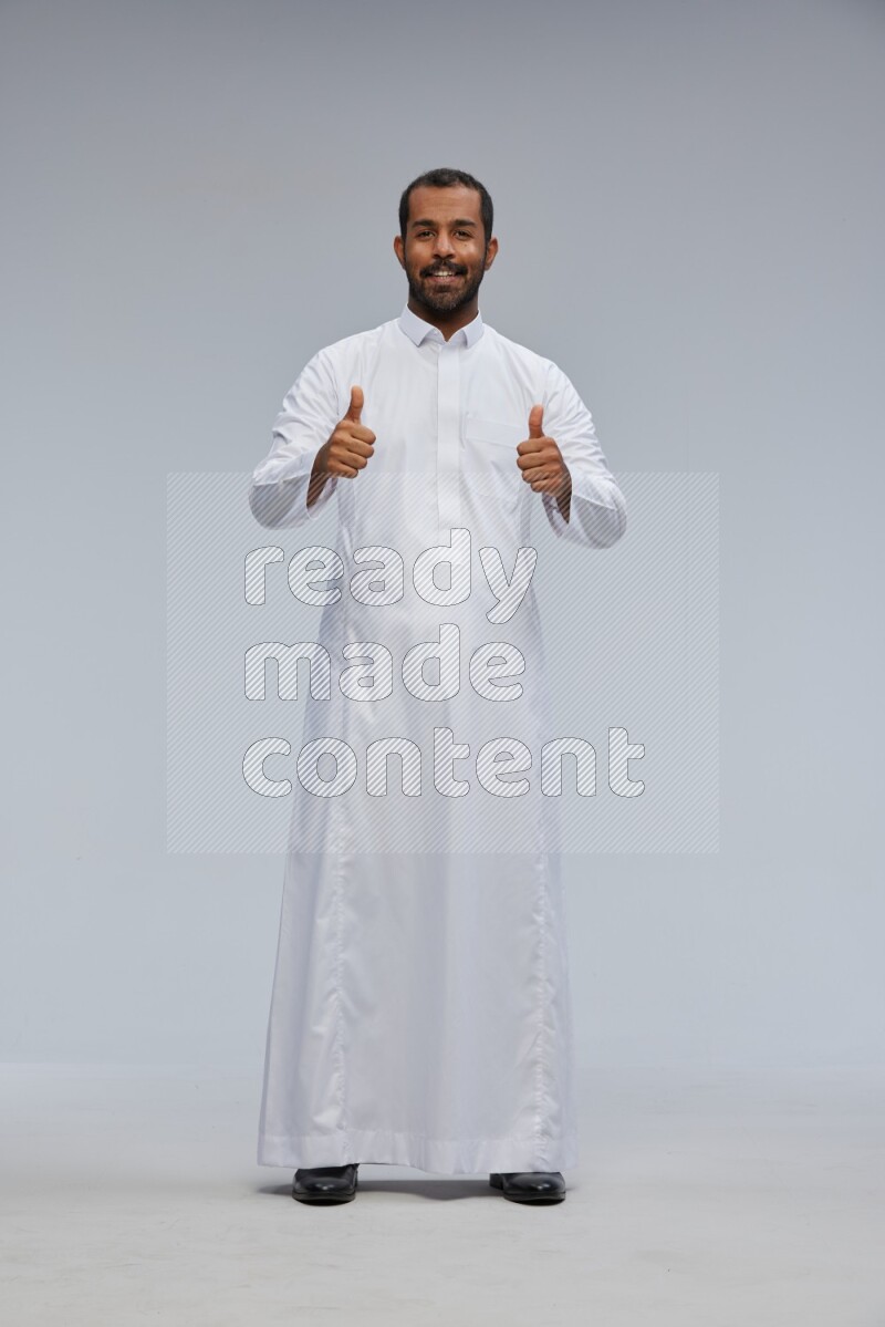 Saudi man Wearing Thob standing interacting with the camera on Gray background