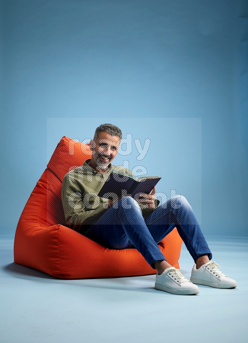 A man sitting on an orange beanbag and reading a book