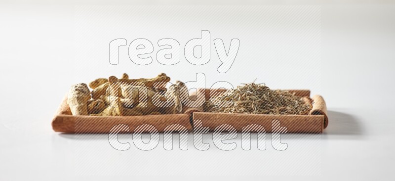 مربعان من أعواد القرفة ممتلئان بحبوب الكمون وأصابع الكركم علي خلفية بيضاء