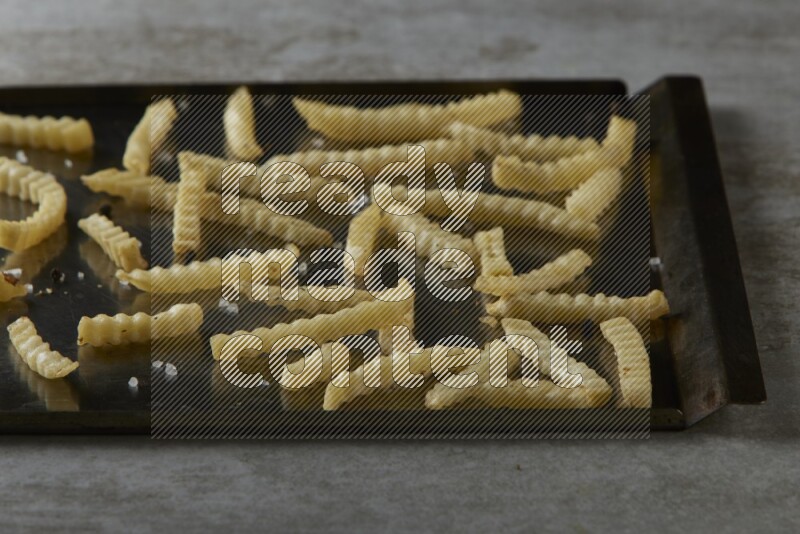 crinkle fries in a black stainless steel rectangle tray on grey textured counter top