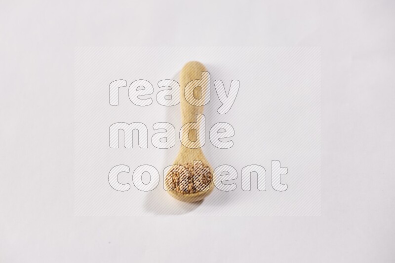 ملعقة خشبية ممتلئة ببذور الخردل علي خلفية بيضاء