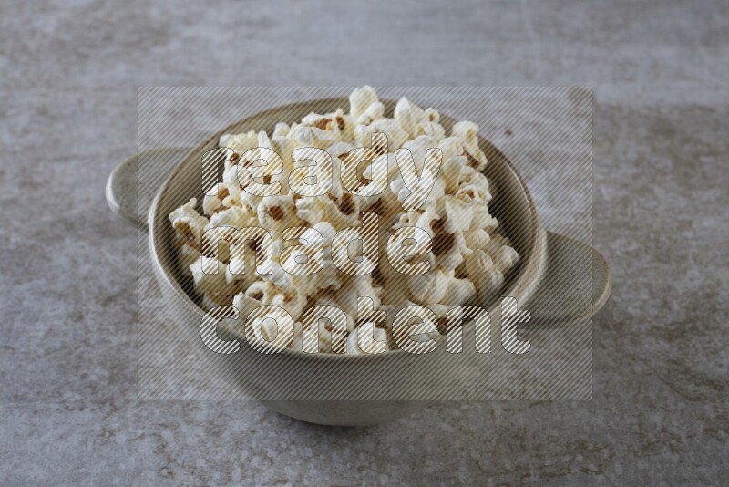 popcorn in a off-white handheld ceramic bowl on a grey textured countertop