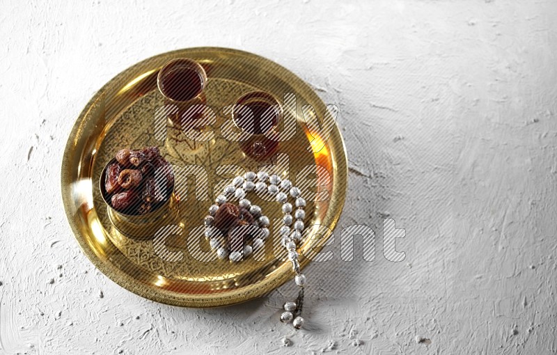 Dates in a metal bowl with tea and prayer beads on a tray in a light setup