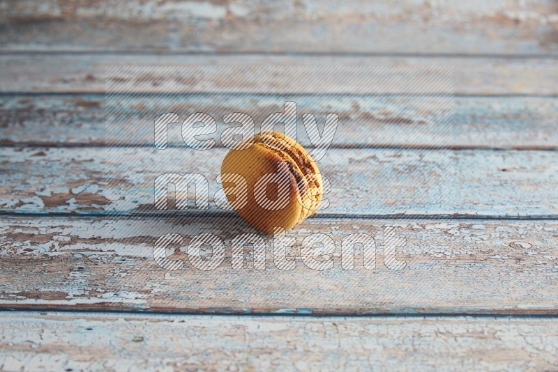45º Shot of Yellow Crème Brulée macaron on light blue wooden background