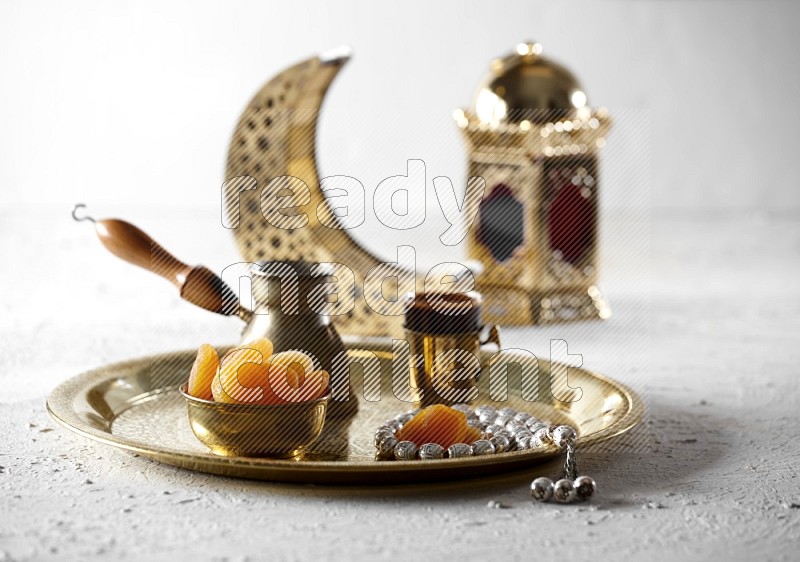 مشمش مجفف في وعاء معدني مع قهوة وسبحة على صينية بجانب فوانيس علي خلفية بيضاء