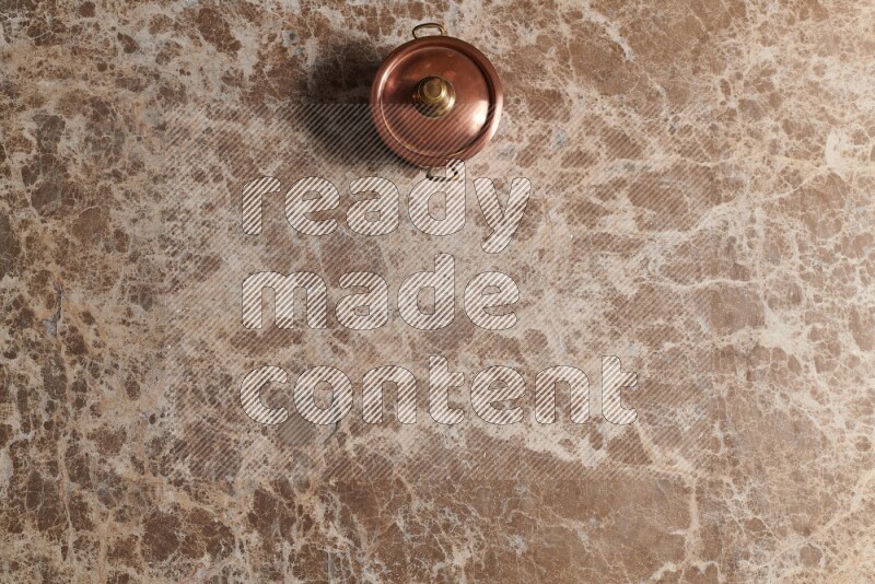 A small copper pot on beige marble background