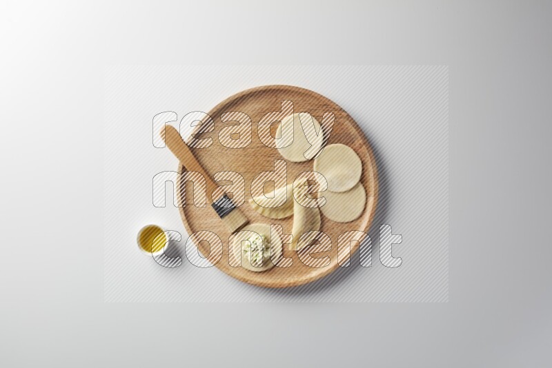two closed sambosas and one open sambosa filled with cheese while oil with oil brush aside in a wooden dish on a white background