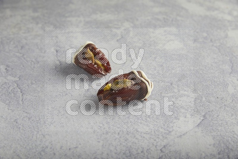 two pistachio stuffed dates covered with dark chocolate with white chocolate drizzle on a light grey background
