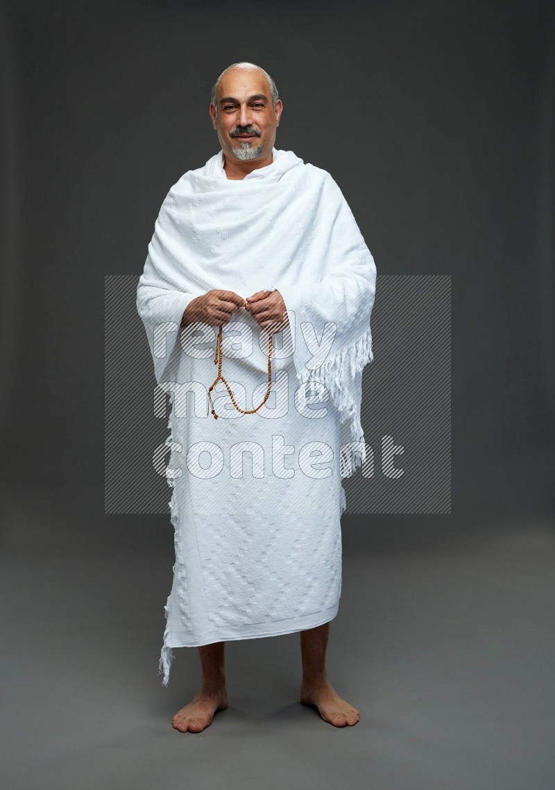 A man wearing Ehram Standing holding rosary on gray background