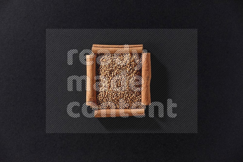 A single square of cinnamon sticks full of mustard seeds on black flooring