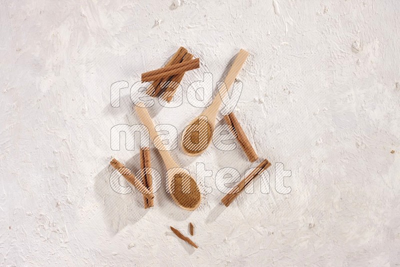 Two wooden spoons full of cinnamon powder with cinnamon sticks on white background