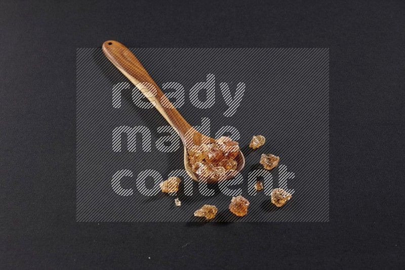 A wooden ladle filled with gum arabic on black flooring