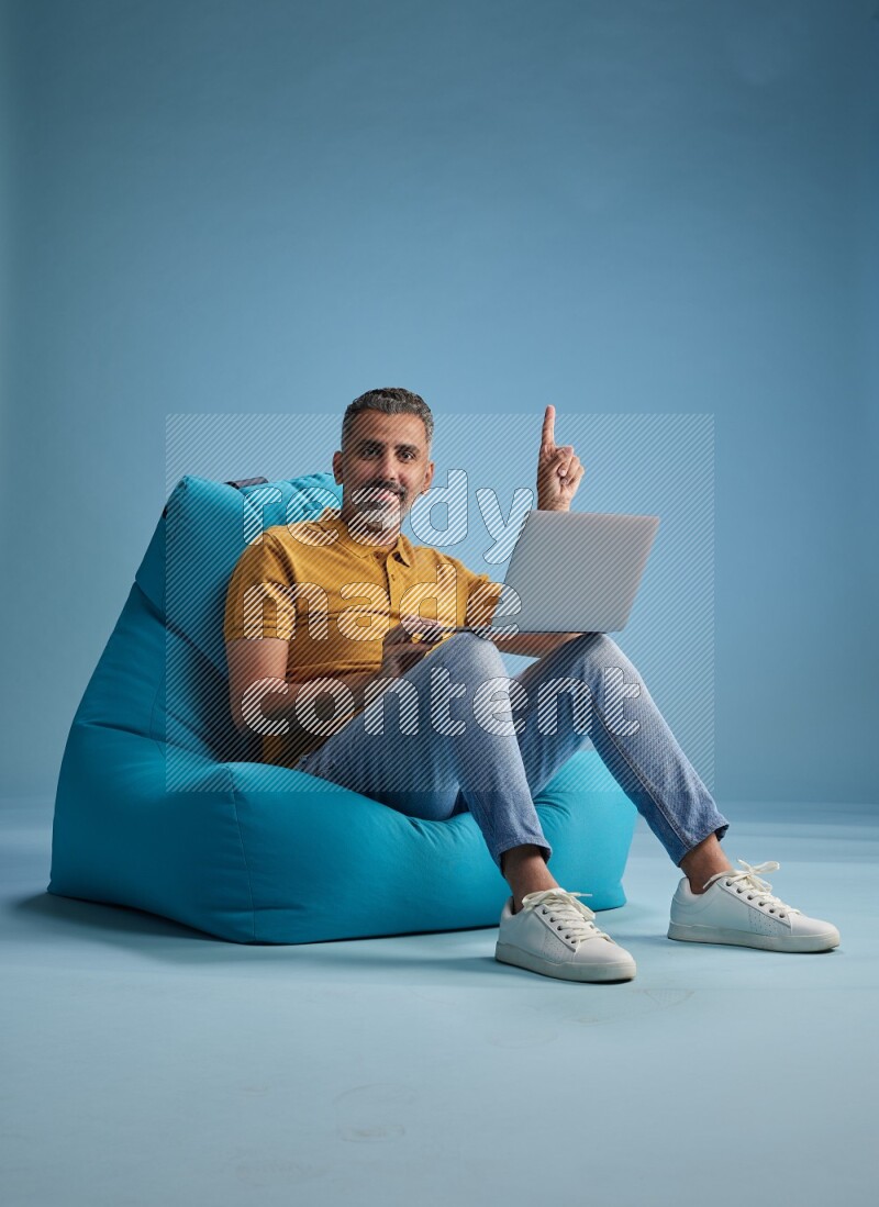 A man sitting on a blue beanbag and working on laptop