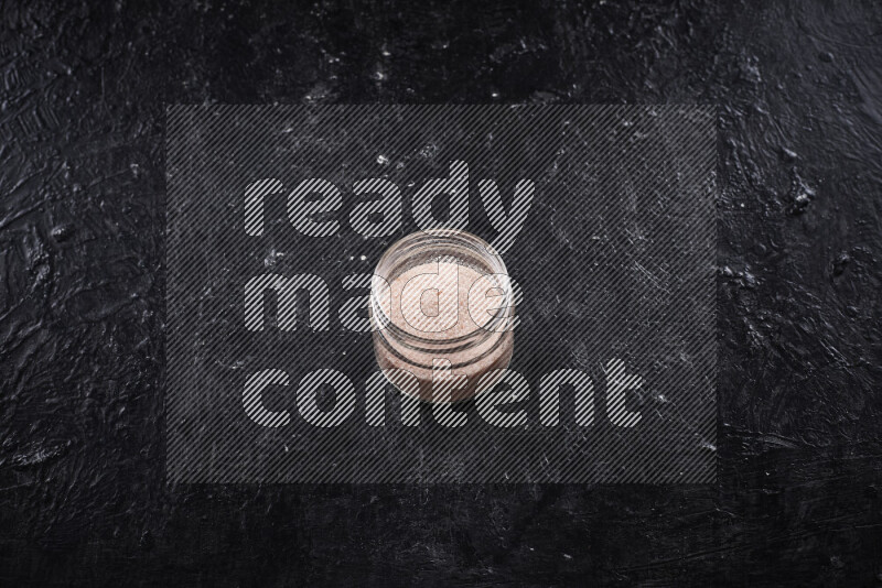 A glass jar full of fine himalayan salt on black background