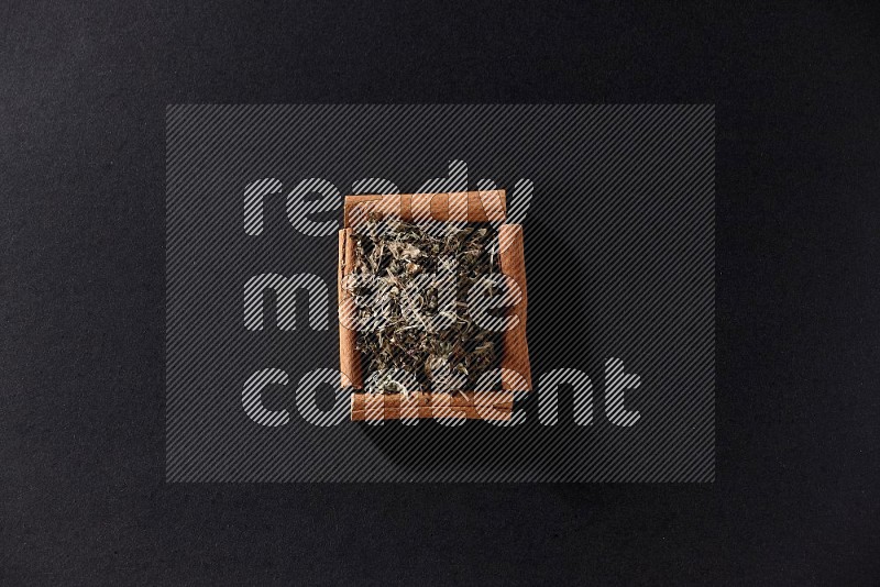 A single square of cinnamon sticks full of dried basil on black flooring