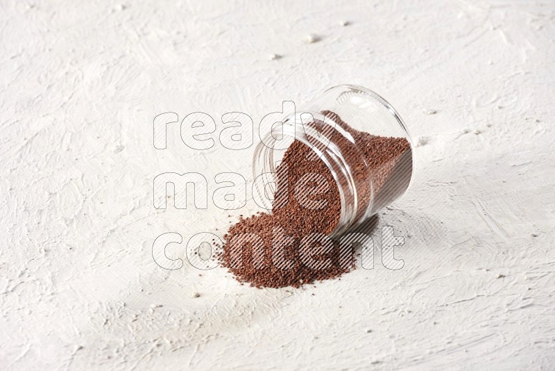 A glass jar full of garden cress seeds and jar is flipped and seeds are spread on a textured white flooring