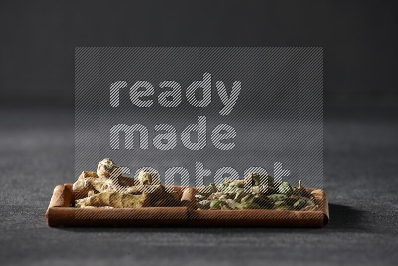 مربعان من أعواد القرفة ممتلئان بحبوب الهيل وأصابع الكركم علي خلفية سوداء