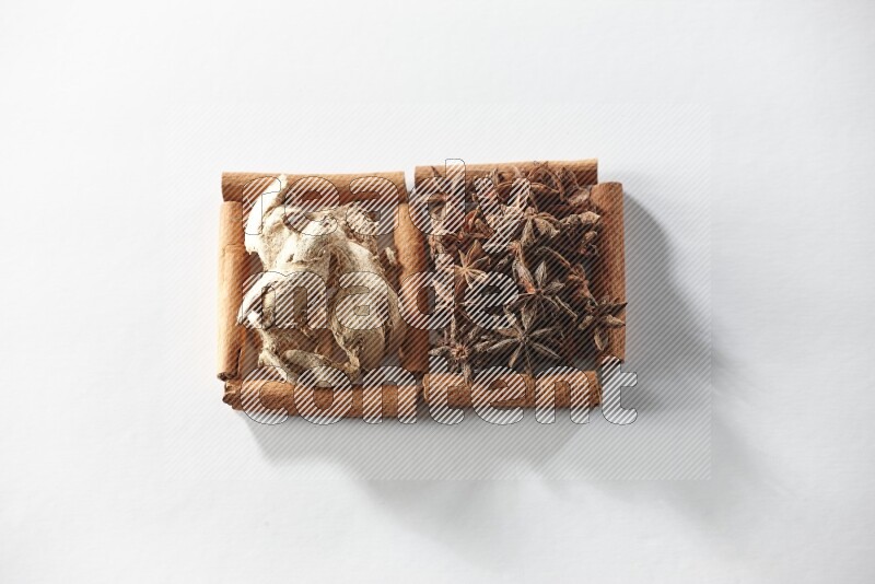 مربعان من أعواد القرفة ممتلئان باليانسون النجمي والزنجبيل المجفف علي خلفية بيضاء