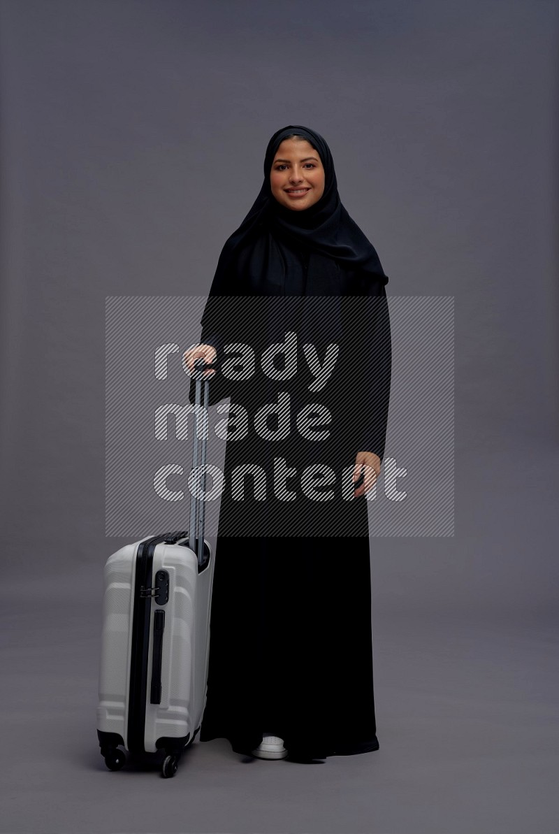 Saudi woman wearing Abaya standing holding bag on gray background