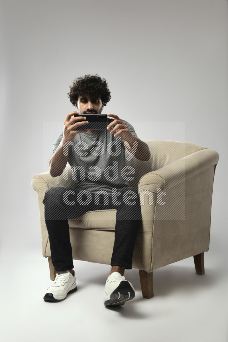 A man wearing casual sitting on a chair shooting with his phone on white background