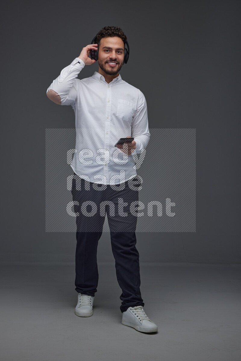 A man wearing smart casual and using his phone and headphone eye level on a gray background