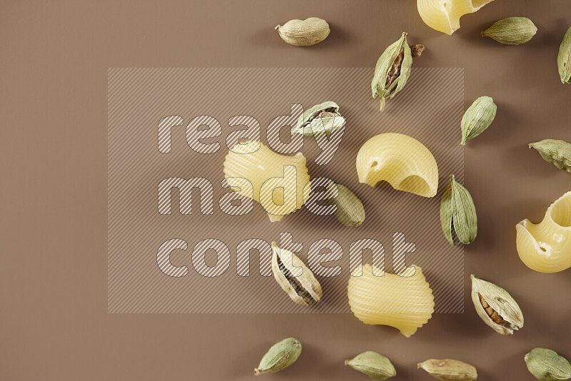 Raw pasta with different ingredients such as cherry tomatoes, garlic, onions, red chilis, black pepper, white pepper, bay laurel leaves, rosemary and cardamom on beige background