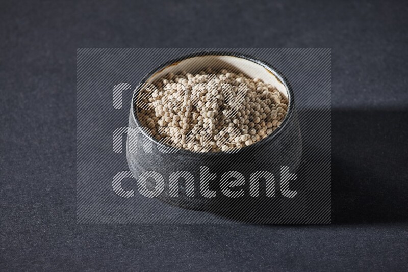 Black pottery bowl full of white pepper on black flooring