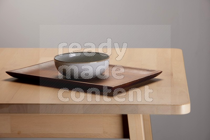 multicolored bowl placed on a rectangular wooden tray on the edge of wooden table